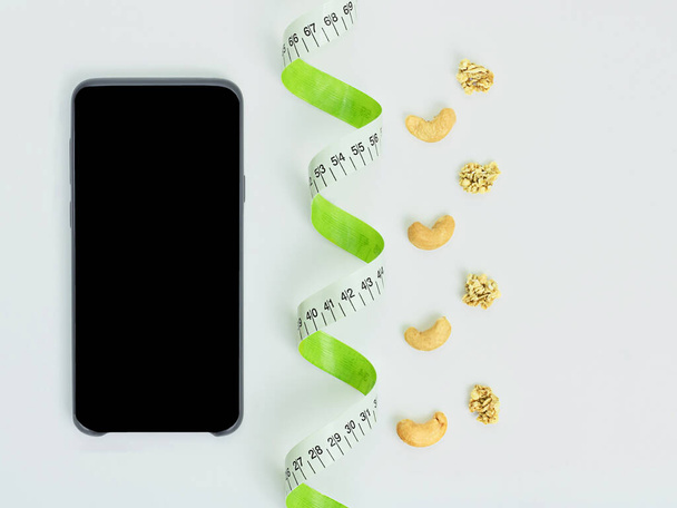 Cinta métrica, smartphone negro, snack saludable, nueces de anacardo - Foto, Imagen