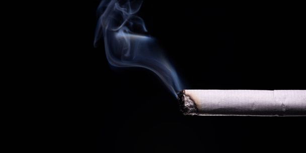 Brandende Sigaret met Rook in een zwarte achtergrond. - Foto, afbeelding