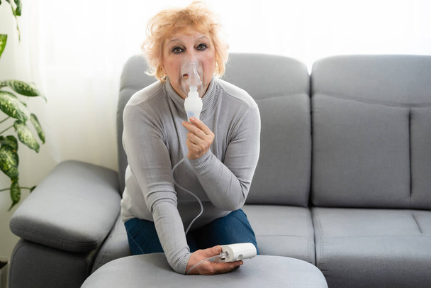 Elderly woman using asthma machine on light background - Photo, Image