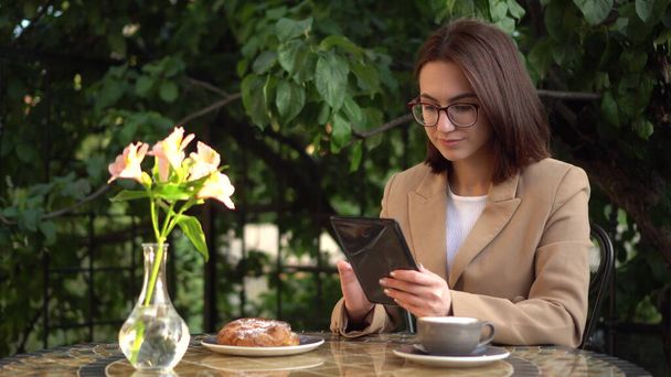 Молодая деловая женщина сидит в кафе и пишет текстовые сообщения на планшете. - Фото, изображение