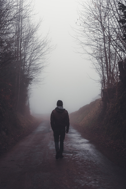 Man loopt alleen over een weg door een donker mistig bos - Foto, afbeelding