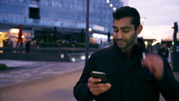Sekarotuinen uros nuori aikuinen juttelemassa tyttöystävä videopuhelu vilkuttaa hyvästit seisoo kaupungissa yöllä - Materiaali, video