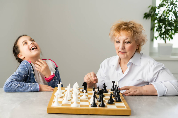 Счастливая девушка с бабушкой, сидящей на диване и играющей в шахматы - Фото, изображение