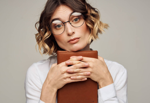 Γυναίκα με ένα σημειωματάριο στα χέρια της και φορώντας γυαλιά σε ένα γκρι φόντο περικοπή άποψη του ένα ελαφρύ πουκάμισο - Φωτογραφία, εικόνα