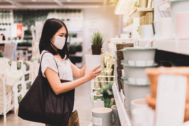 Beautiful asian woman wearing surgical face mask and shopping during virus outbreak in garden shop - Foto, imagen