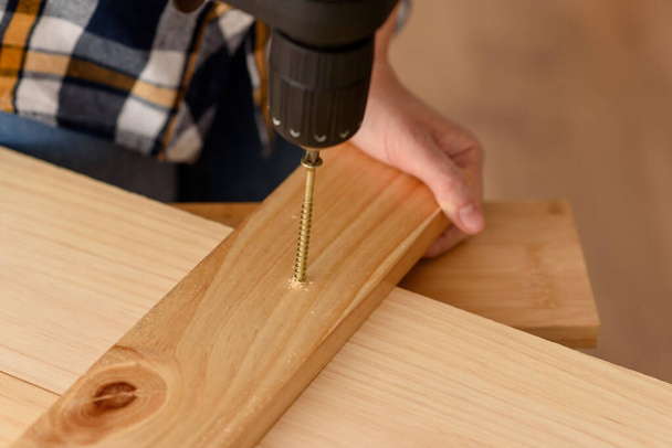 Close up of a drill drilling a screw into a piece of wood, on a wooden bench. Woman working on wooden bench. DIY enthusiast. - Photo, Image