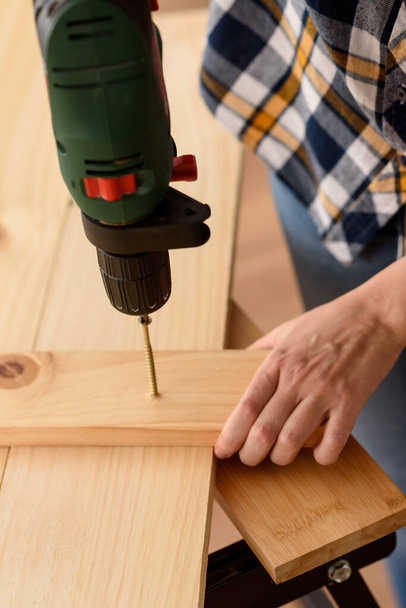 Close up of a drill drilling a screw into a piece of wood, on a wooden bench. Woman working on wooden bench. DIY enthusiast. - Photo, Image