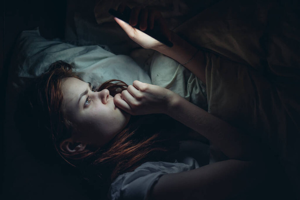 nainen makuuhuoneessa puhelin käsissään makaa sängyssä kommunikoi - Valokuva, kuva