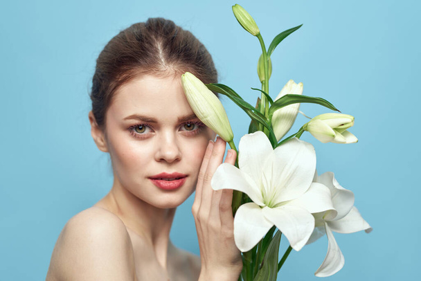 白い花を持つ女性上の青い背景クロップドビューの裸の肩 - 写真・画像