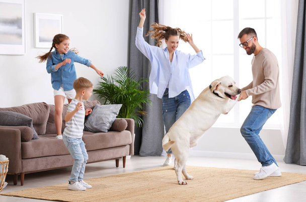 幸せな遊び心のある家族の完全な体:かわいい純血種を持つ親と小さな子供ラブラドールの検索犬自宅のリビングルームで一緒に楽しさと踊りを持つ - 写真・画像
