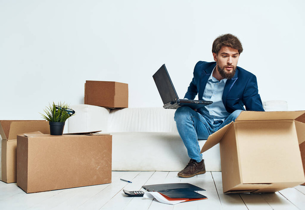 Geschäftsmann mit Laptop sitzt auf Sofa und packt Kisten aus - Foto, Bild