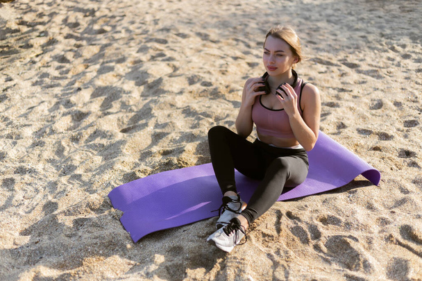 Atrakcyjna fitness kobieta siedzi na macie na plaży. Zdrowy styl życia - Zdjęcie, obraz