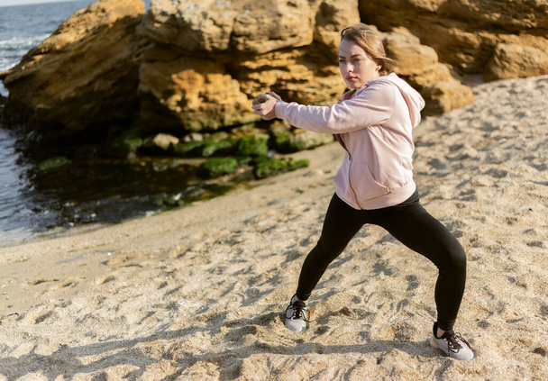 Mujer de fitness haciendo ejercicio con una piedra en una playa salvaje. Estilo de vida saludable, concepto de fitness - Foto, imagen