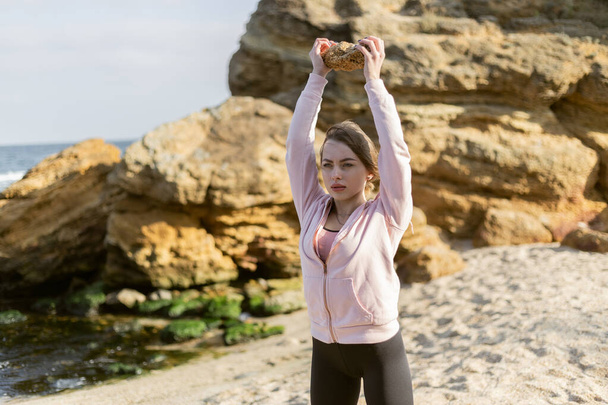 Fitness woman exercising with a stone on a wild beach. Healthy lifestyle, fitness concept - 写真・画像