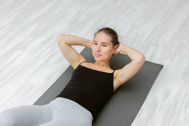Joven mujer en forma atractiva entrena los músculos abdominales mientras está acostado en la alfombra y haciendo crujidos en el suelo - Foto, imagen