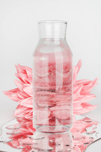 рожеві квіти, спотворені через воду в пляшці з дзеркалом на синьому фоні. чиста вода, розслабтеся, сюрреалістична, екологічно чиста домашня концепція. копіювання простору
 - Фото, зображення