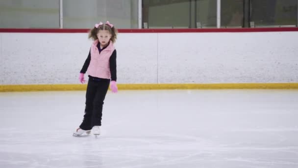 Klein meisje oefenen figuur schaatsen beweegt op een indoor ijsbaan. - Video