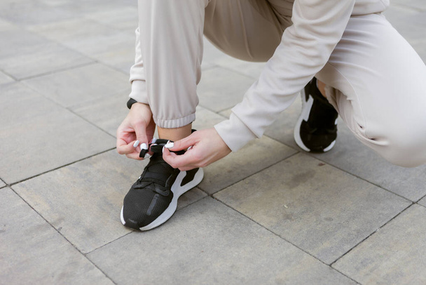 Mujer con ropa deportiva ata los cordones de las zapatillas al aire libre - Foto, imagen