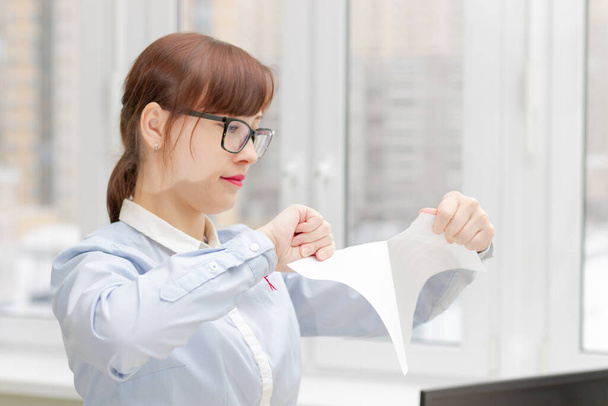 junge hübsche Geschäftsfrau in streng stylischer Kleidung und Brille im Büro in der Nähe des Desktops, die Dokumente zerreißt - Foto, Bild