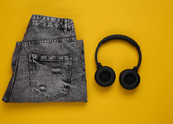 Jeans and headphones on a yellow background. Clothing and accessories. Urban style, travel concept. Top view - Photo, Image