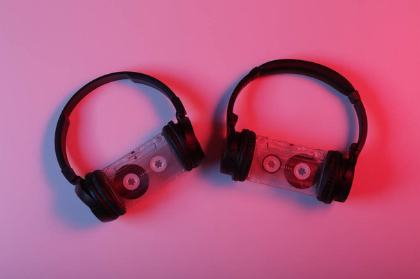 Twee paar zwarte stereo koptelefoons en audiocassette in rood blauw neon licht - Foto, afbeelding
