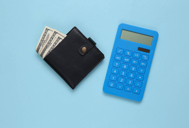 Cartera de cuero con billetes de cien dólares y calculadora sobre fondo azul. Ahorro de dinero - Foto, imagen
