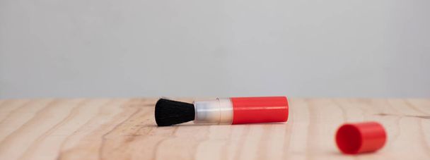 Černý štětinatý objektiv čistící štětec s červeným barevným klipem na dřevěném stole ležel plochý. - Fotografie, Obrázek