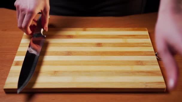 Female hands stack on a wooden board on the table metal kitchen utensils - a knife, a grater in the form of a platen, a sieve mug for flour and a double-sided knife for cutting pizza and dough - Footage, Video