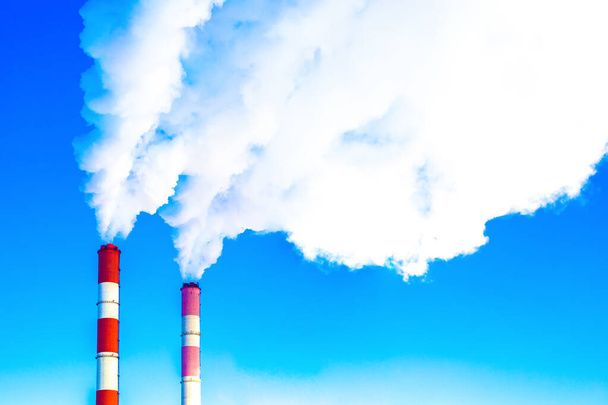 Schoorstenen van een fabriek die de blauwe lucht vervuilt. Grote witte rookwolken in een helderblauwe lucht, horizontale fotografie - Foto, afbeelding