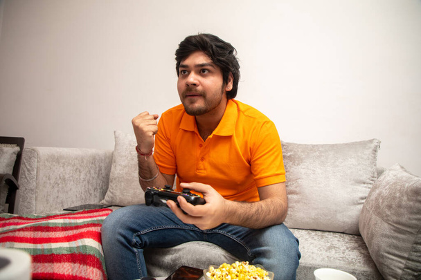Asiatique indien homme jeu, streaming et regarder la télévision seul dans le salon sur un canapé gris et une table blanche. - Photo, image