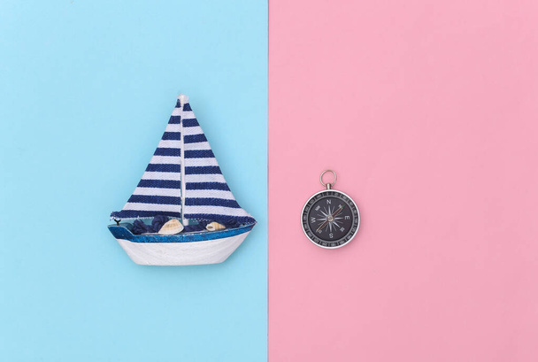 Zeilboot en kompas op een blauwe roze achtergrond. Reizen, minimalisme concept. Bovenaanzicht. Vlakke plaat - Foto, afbeelding