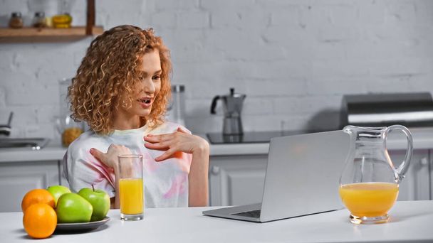 kihara nuori nainen osoittaa itseään puhuessaan videopuhelun aikana keittiössä  - Valokuva, kuva