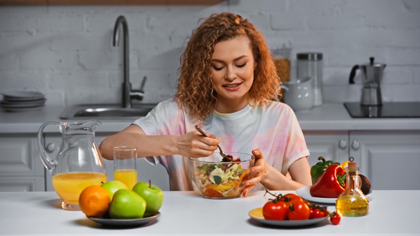 Fröhliche Frau blickt auf frischen Salat in Schüssel  - Foto, Bild