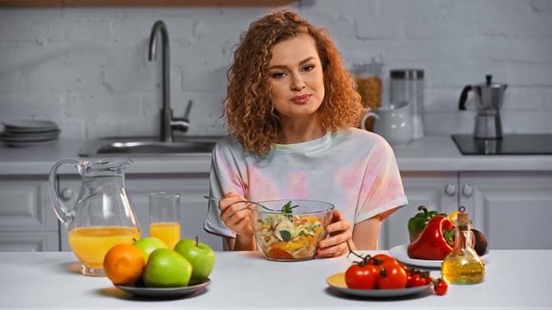Fröhliche Frau hält Gabel neben frischem Salat in Schüssel  - Foto, Bild