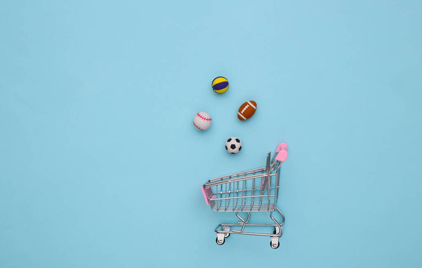 Mini shopping cart with different sport balls on a blue background. Top view - Photo, Image