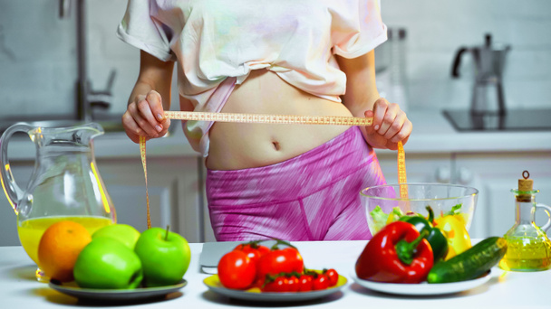 visión parcial de la mujer midiendo la cintura cerca de verduras y frutas en primer plano borroso - Foto, Imagen