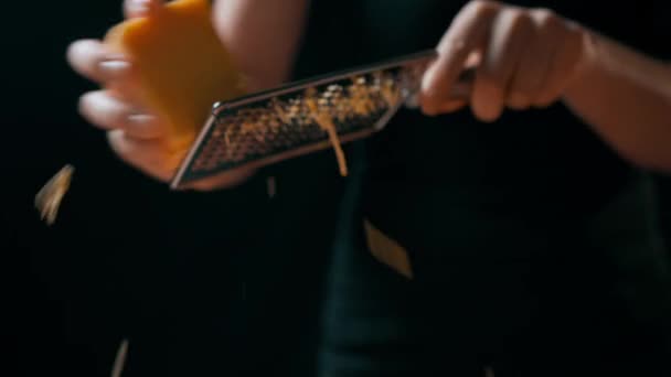 Een jong meisje in een zwart uniform houdt een rasp in de vorm van een metalen plaat in zachte schone handen en maalt er harde kaas op. Keukenapparatuur, gereedschap, inventaris. Heerlijke zuivelgerechten - Video