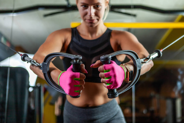Giovane donna in forma bionda eseguire esercizio con macchina esercizio Cable Crossover in palestra. Focus sulle mani - Foto, immagini
