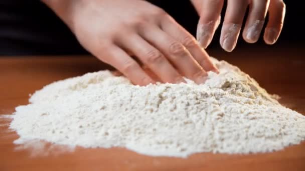 Las manos de una joven caucásica sobre una mesa de madera desenrollan una pila de harina blanca y hacen en el medio del recreo para romper un huevo allí y luego la mujer sacude el polvo de la harina de sus manos - Metraje, vídeo