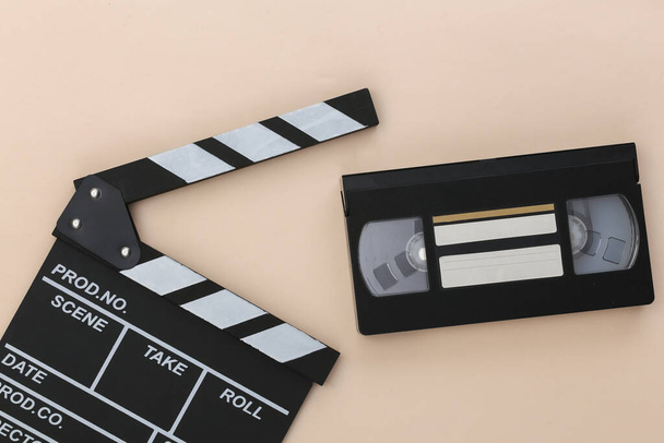 Filmklappbrett und Videokassette auf beigem Hintergrund. Kinobranche, Unterhaltung. Ansicht von oben - Foto, Bild