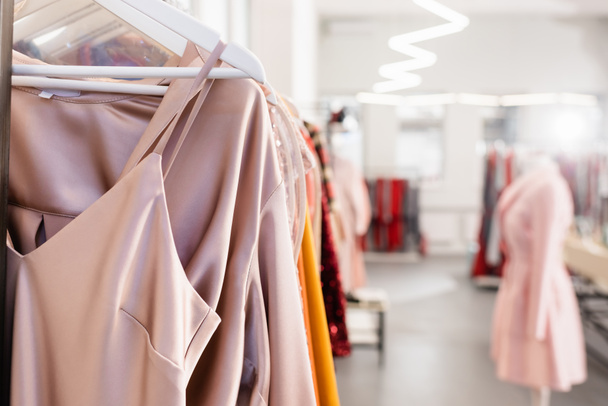 Stilvolle Klamotten auf Kleiderbügeln im Showroom vor verschwommenem Hintergrund  - Foto, Bild