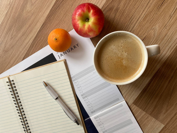 Arbeitsplatz mit Kalender, Notizbuch, Stift, Kaffee und gesunden Fruchtsnacks auf dem Schreibtisch. - Foto, Bild