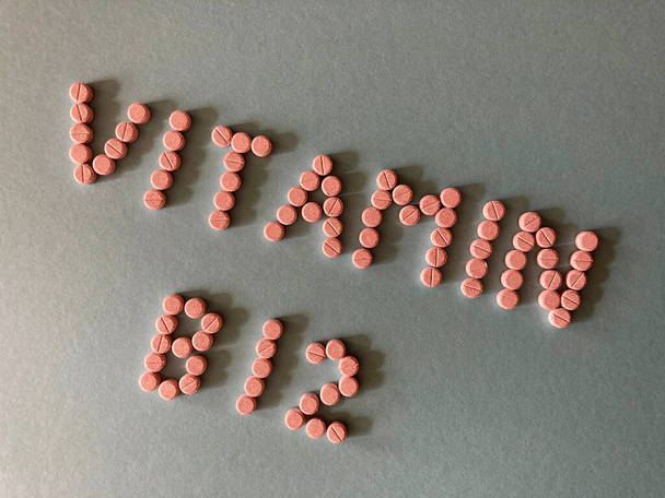 Vitamina B12, palabras en pequeñas tabletas de color rosa aisladas en el fondo - Foto, Imagen