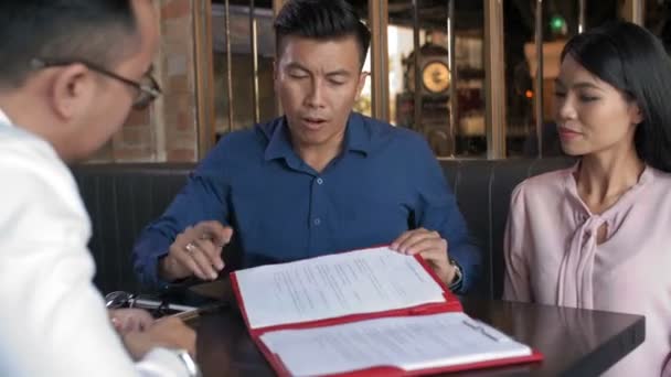 Mittlere Aufnahme von drei asiatischen Geschäftspartnern, die im Restaurant sitzen und über den Vertrag diskutieren - Filmmaterial, Video