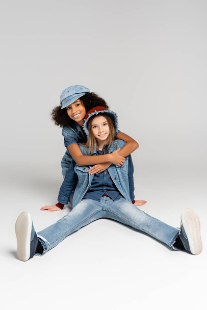 радісна афроамериканська дівчина обіймає щасливого, стильного друга, що сидить на сірому
 - Фото, зображення