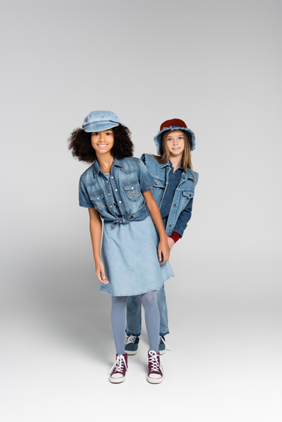 full length view of stylish interracial girls in trendy clothes and gumshoes posing on grey - Foto, immagini