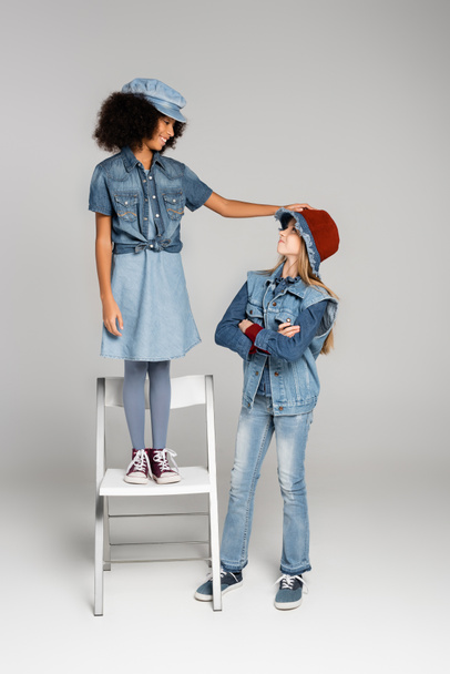 stylish african ameican girl standing on chair near friend on grey - Photo, image