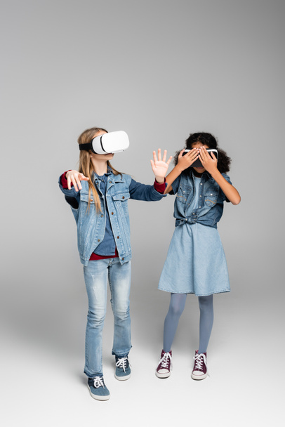 african american girl covering vr headset while standing near friend on grey - Фото, зображення