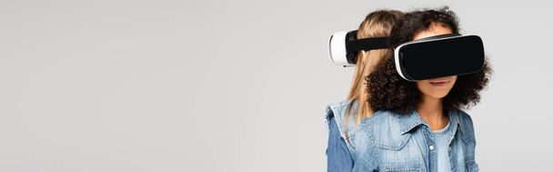 interracial girls in denim clothes and vr headsets isolated on grey, banner - Фото, зображення