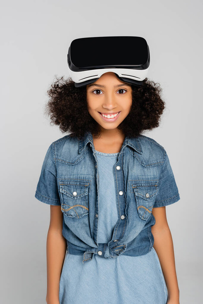 joyful african american girl in stylish clothes and vr headset looking at camera isolated on grey - Photo, Image